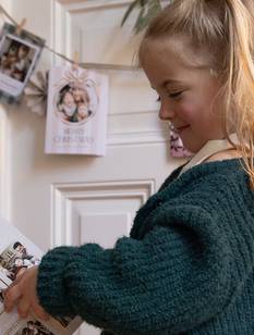 Kleines Mädchen im weihnachtlich geschmückten Wohnzimmer schaut sich Weihnachtskarte an