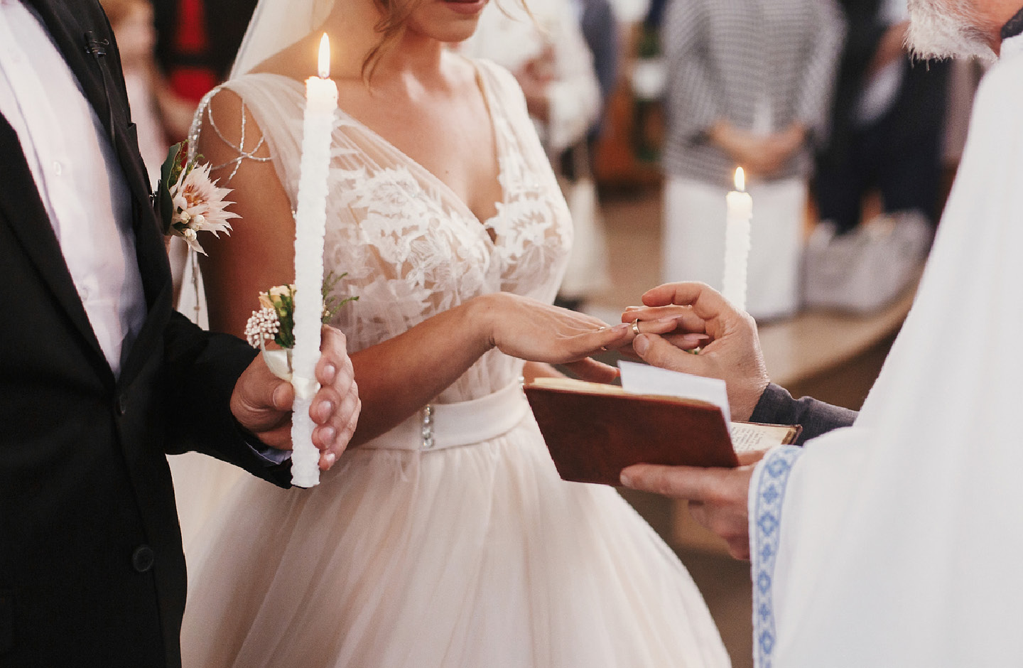 Brautpaar vor dem Pfarrer, mit Kerzen in der Hand, Der Pfarrer steckt der Braut den Ring an den Finger