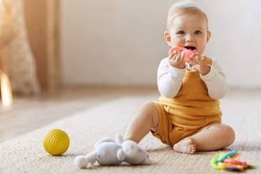 Baby sitzt auf dem Teppich und spielt mit einem rosa Beißring