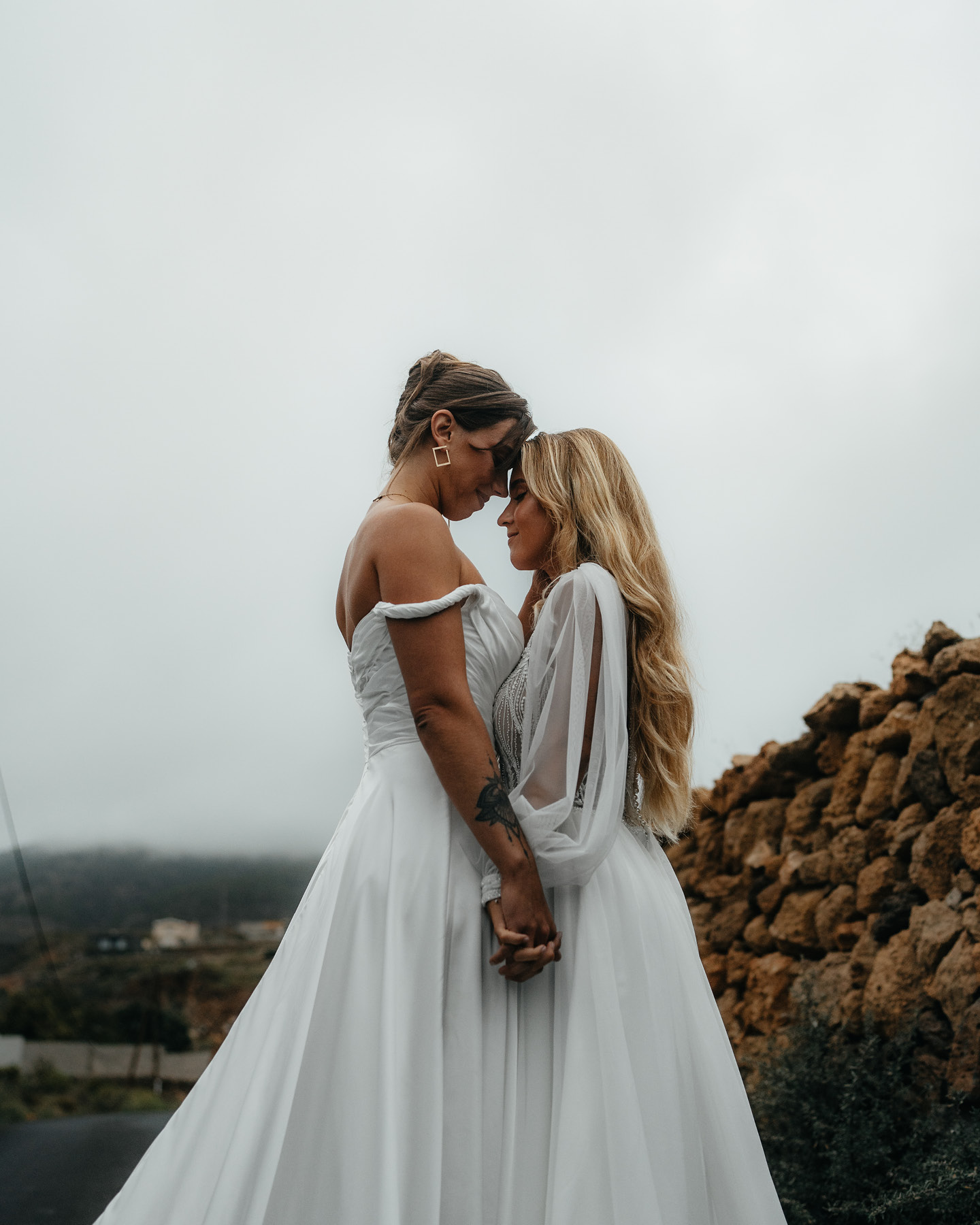 Zwei Bräute in Hochzeitskleidern, einander zugewandt  in zärtlicher Pose