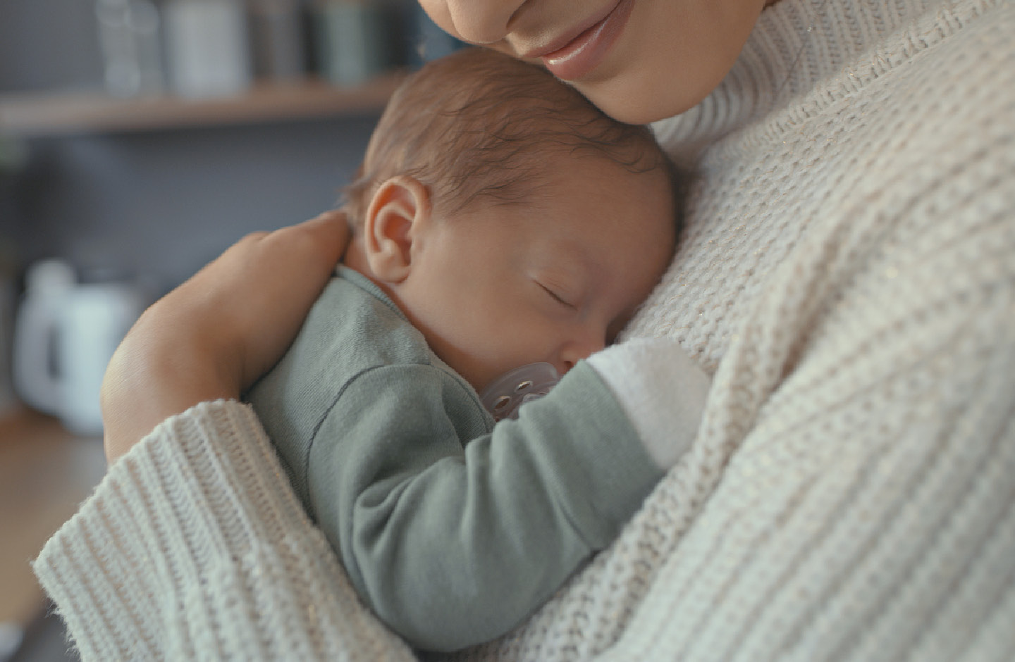 Bildausschnitt von lächelnder Mutter mit schlafendem Baby auf dem Arm