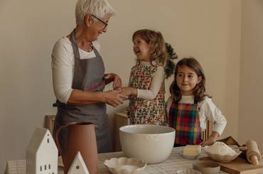 Oma mit ihren zwei Enkelinnen an einem Tisch mit Backzutaten