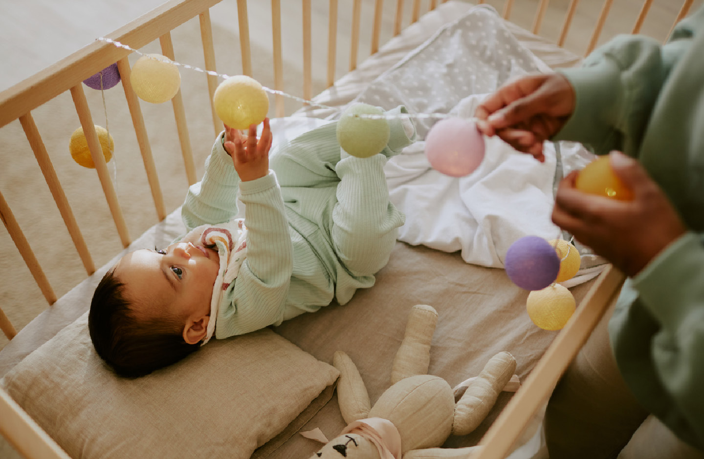 Baby im Babybett spielt mit einer Ballkette, die über das Bett gespannt ist