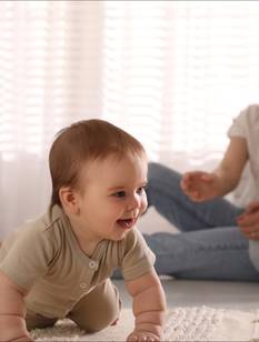 Baby krabbelt auf dem Boden, im Hintergund lachende Eltern