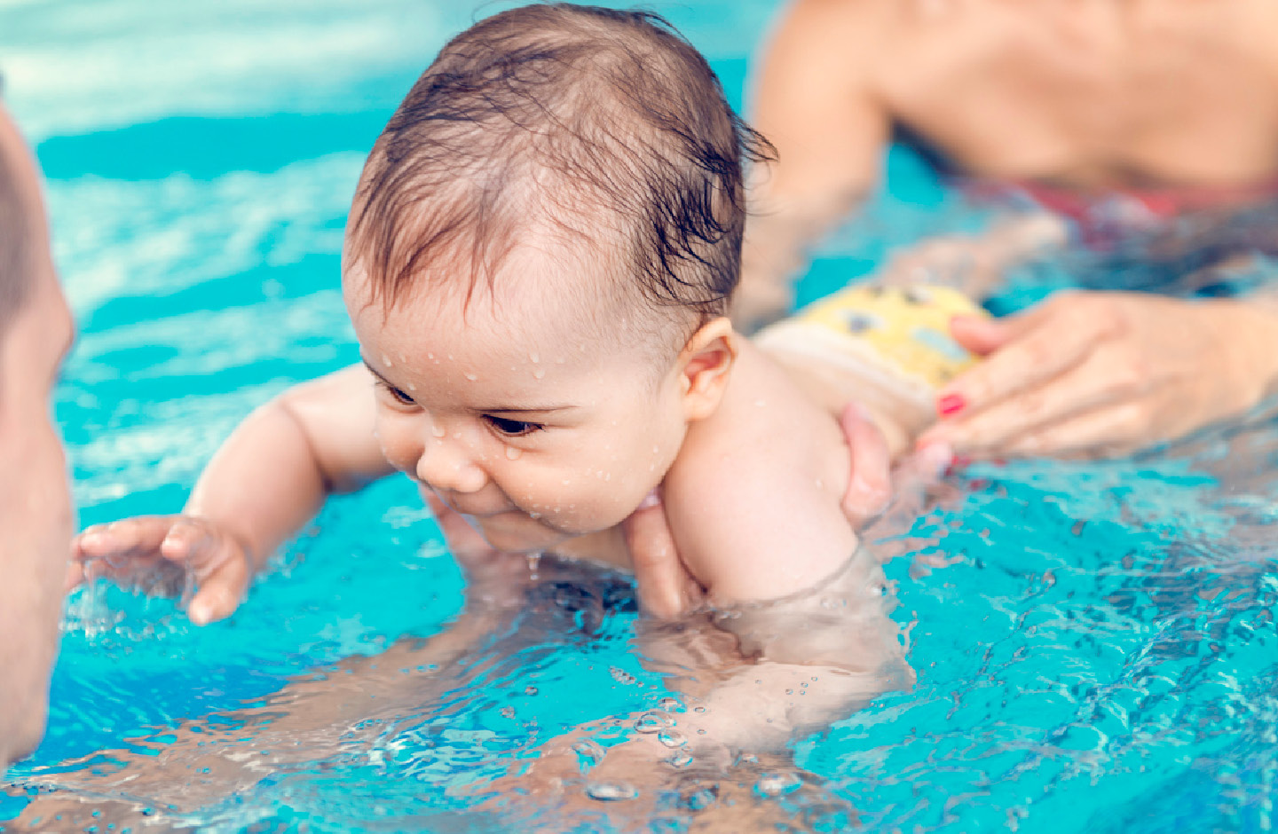 Baby mit Schwimmmeister und Mutter im Schwimmbad