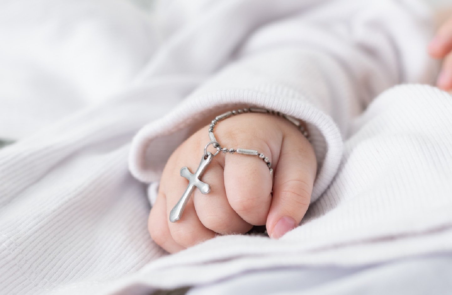 Babyhand mit silbernem Kreuz an einer Kette